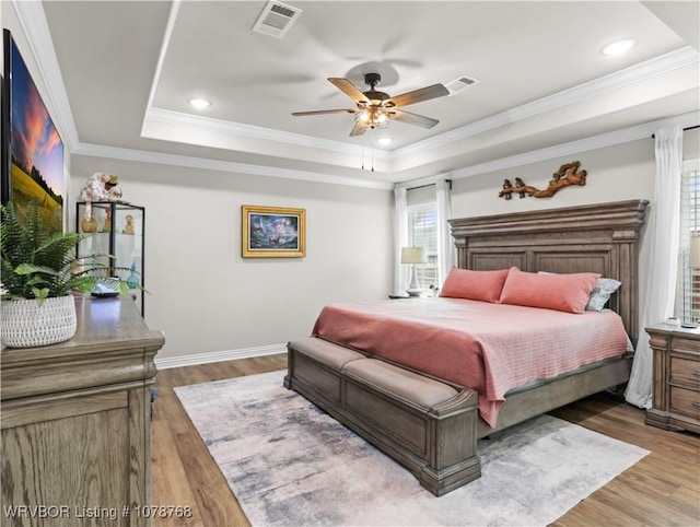 bedroom featuring wood-type flooring, ornamental molding, ceiling fan, and a tray ceiling