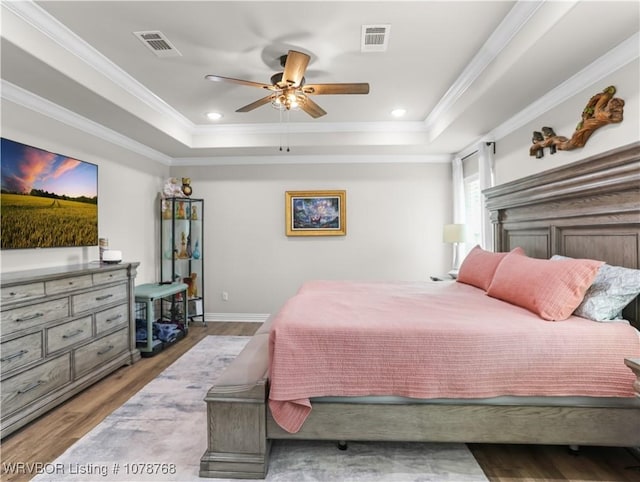 bedroom with crown molding, ceiling fan, light hardwood / wood-style floors, and a tray ceiling