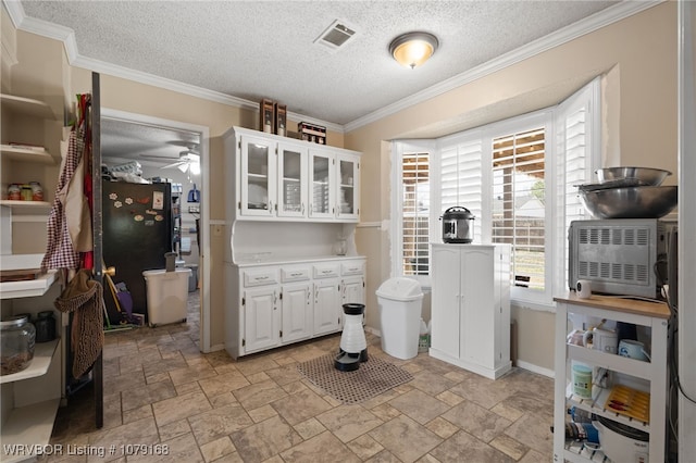 interior space featuring freestanding refrigerator, stone tile flooring, visible vents, and white cabinetry