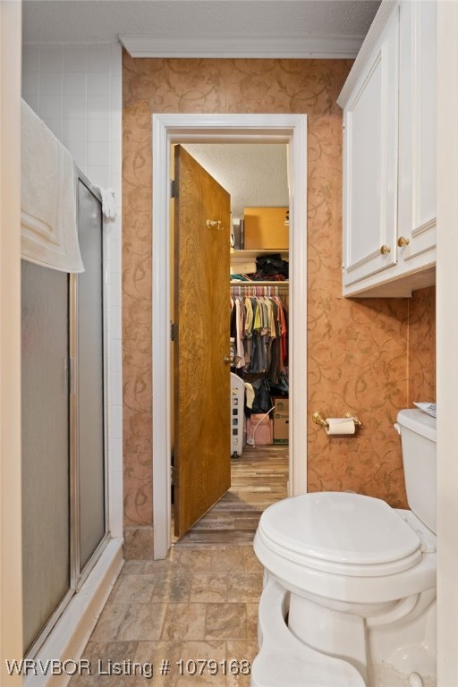 bathroom featuring a spacious closet, a shower stall, toilet, and wallpapered walls