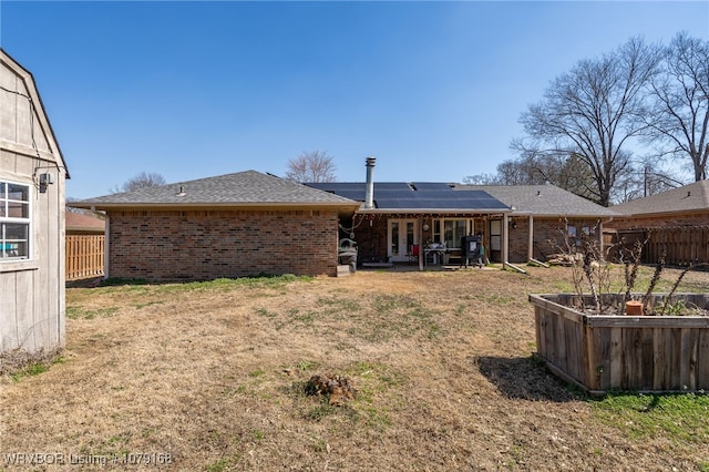 rear view of house featuring solar panels, brick siding, fence, a yard, and french doors