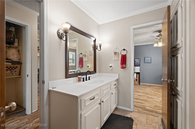 bathroom with a textured ceiling, ceiling fan, stone tile floors, vanity, and ornamental molding