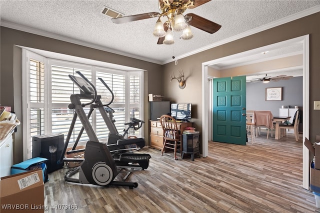 exercise area featuring a textured ceiling, wood finished floors, a ceiling fan, visible vents, and crown molding