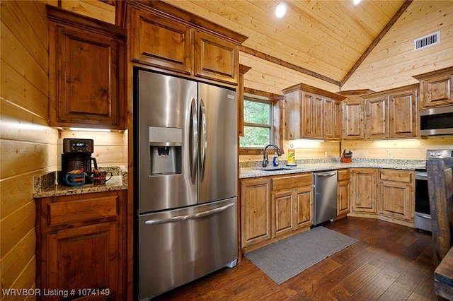 kitchen featuring stainless steel appliances, light stone counters, dark hardwood / wood-style floors, and wooden walls