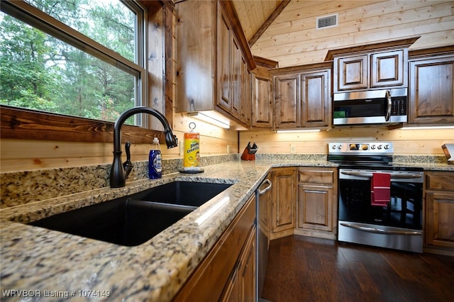 kitchen featuring wood walls, dark wood-type flooring, sink, light stone counters, and stainless steel appliances