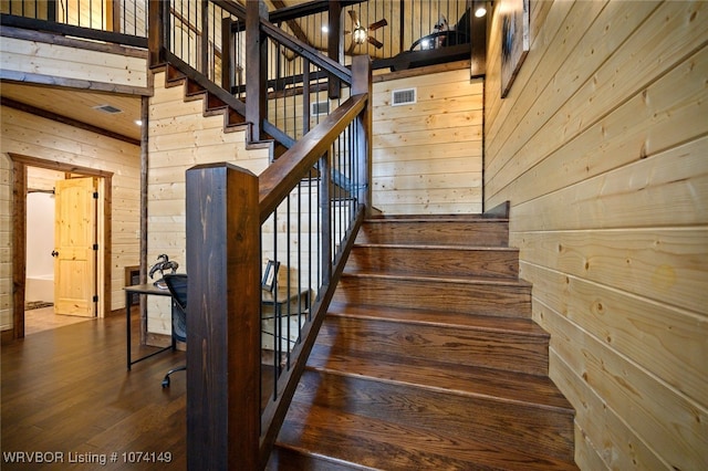 stairs with hardwood / wood-style flooring, ceiling fan, and wooden walls