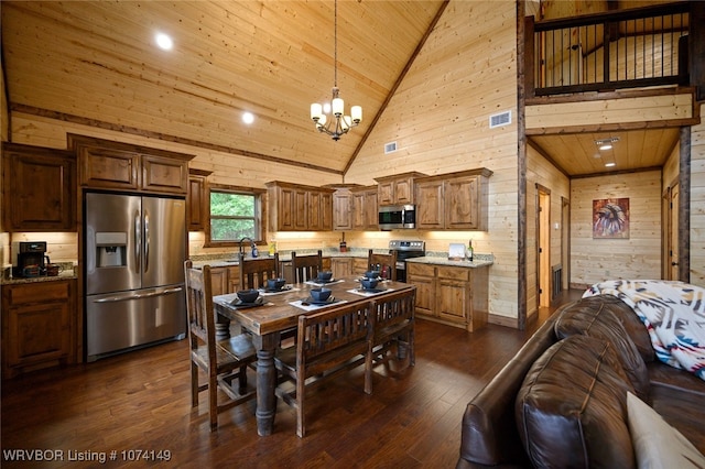 kitchen with decorative light fixtures, stainless steel appliances, high vaulted ceiling, and wood walls