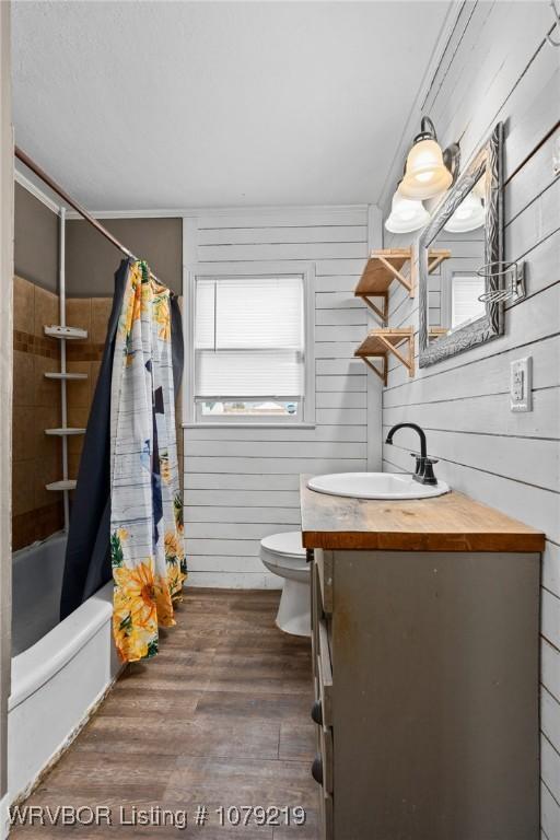 bathroom featuring shower / tub combo, wooden walls, toilet, wood finished floors, and vanity