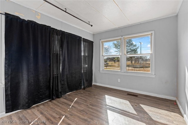 spare room with wood finished floors, visible vents, and baseboards