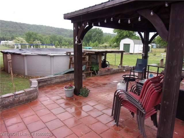 view of patio / terrace with a storage unit, a forest view, an outbuilding, and an outdoor pool