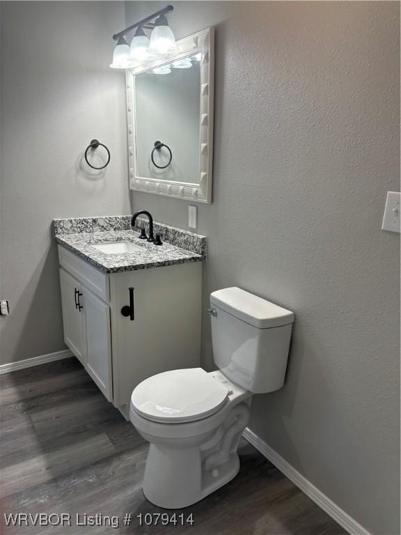 half bathroom with vanity, wood finished floors, toilet, and baseboards