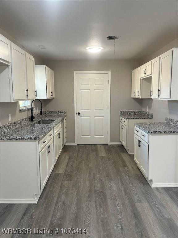 kitchen with white cabinets, light stone countertops, dark wood-type flooring, and a sink