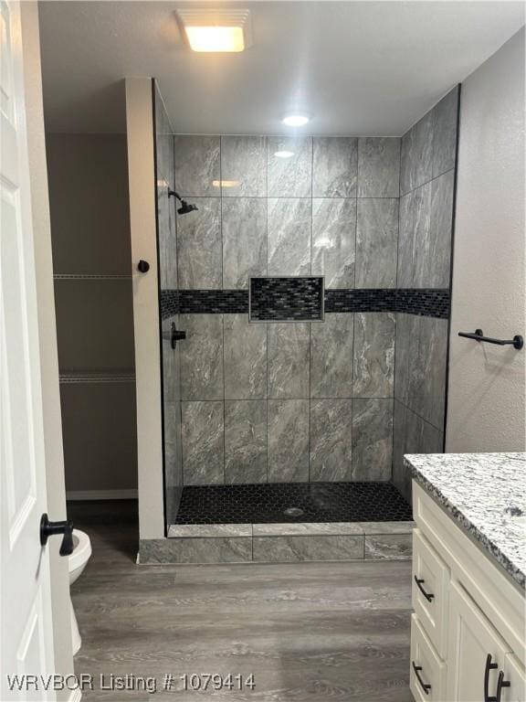 full bathroom featuring toilet, wood finished floors, a tile shower, and vanity