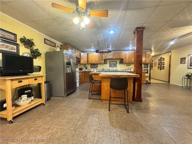 6538 110th Rd, Red Oak, OK 74563 - kitchen featuring a ceiling fan, brown cabinetry, stainless steel appliances, a kitchen bar, and tile patterned flooring