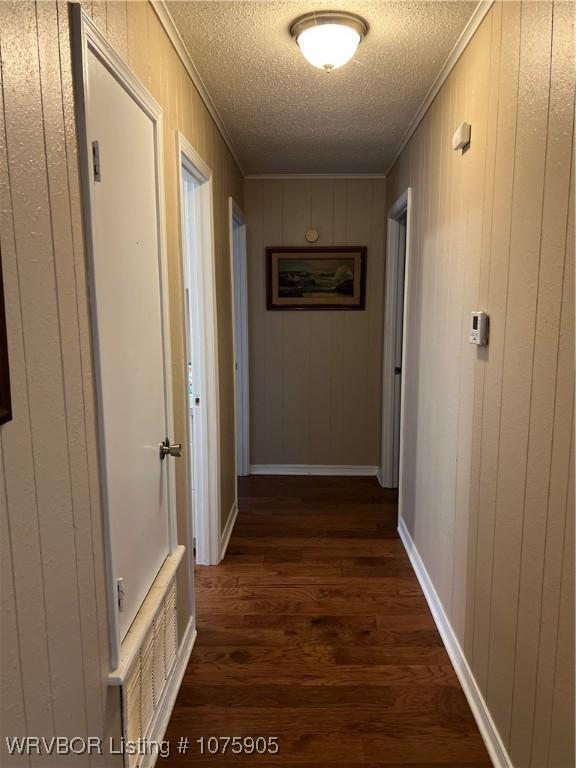 hallway with a textured ceiling, dark hardwood / wood-style flooring, crown molding, and wooden walls