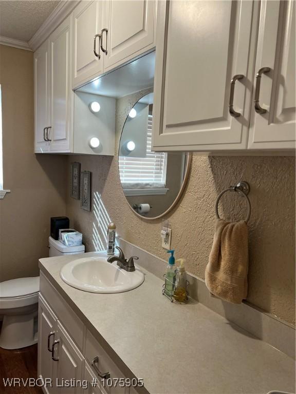 bathroom featuring a textured ceiling, vanity, toilet, and ornamental molding