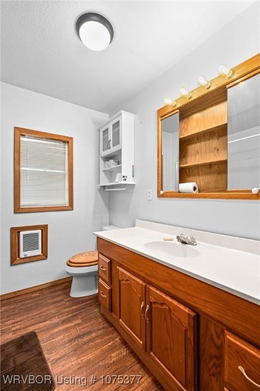 bathroom featuring wood-type flooring, vanity, heating unit, and toilet