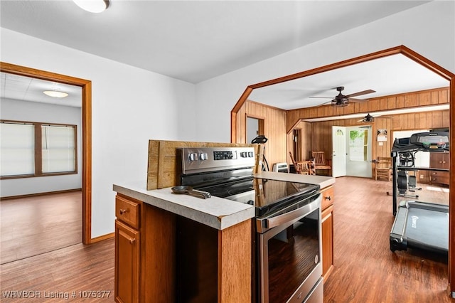 kitchen featuring stainless steel range with electric stovetop, ceiling fan, wood walls, and hardwood / wood-style floors