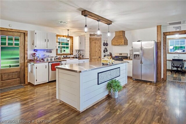 kitchen featuring white cabinetry, hanging light fixtures, stainless steel appliances, a kitchen island, and custom range hood