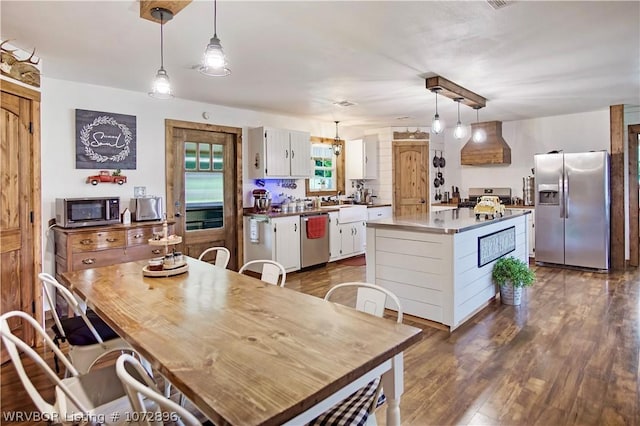 kitchen with a center island, premium range hood, decorative light fixtures, white cabinets, and appliances with stainless steel finishes