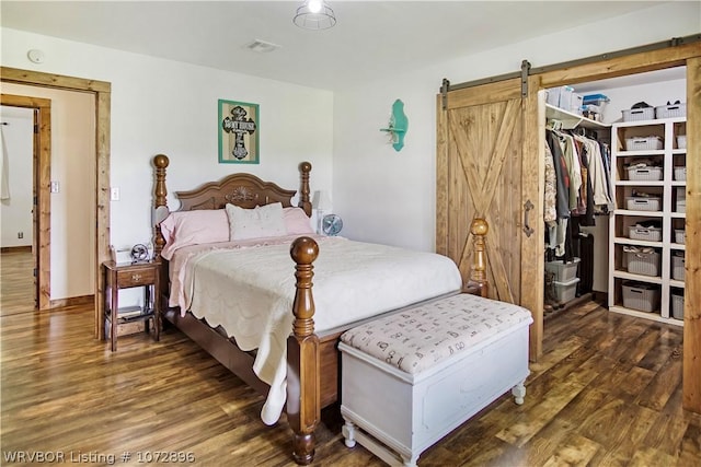 bedroom with a walk in closet, a barn door, a closet, and dark wood-type flooring