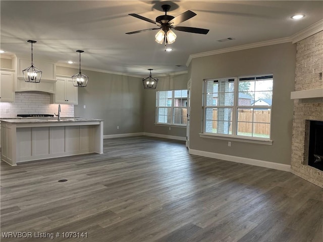 unfurnished living room featuring ceiling fan, crown molding, dark wood-type flooring, sink, and a fireplace