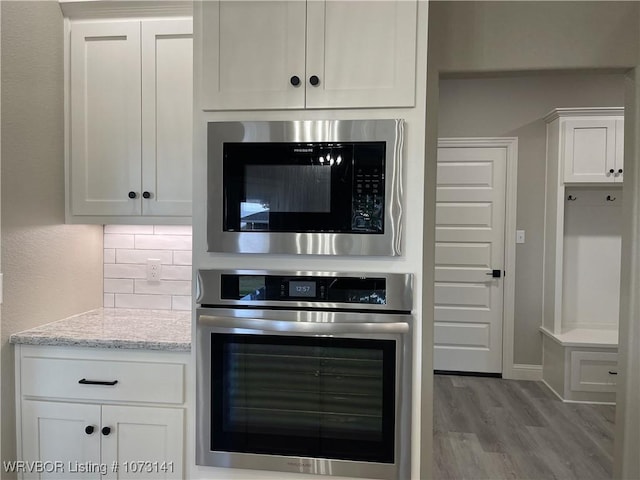 kitchen with stainless steel oven, light stone countertops, white cabinetry, and built in microwave