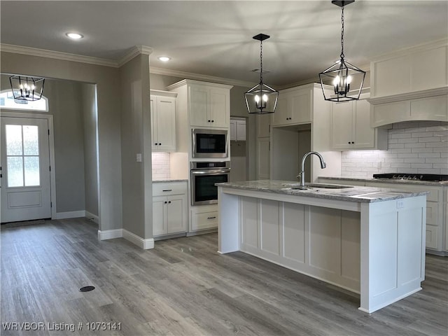 kitchen featuring built in microwave, sink, oven, a center island with sink, and white cabinets