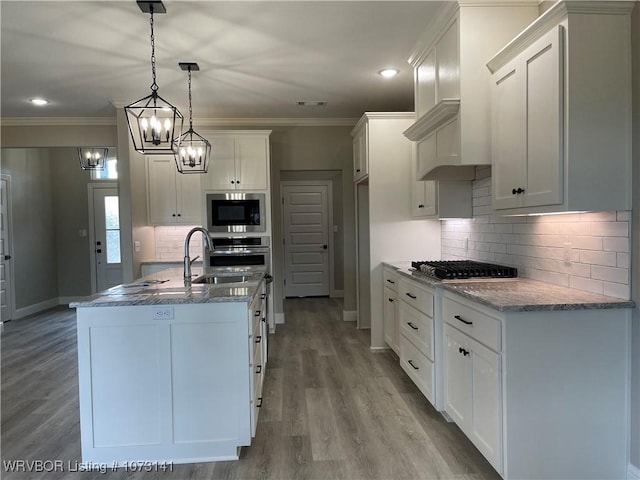 kitchen with stainless steel appliances, a kitchen island with sink, light hardwood / wood-style flooring, white cabinetry, and hanging light fixtures