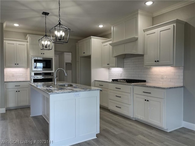 kitchen featuring stainless steel oven, hanging light fixtures, built in microwave, an island with sink, and white cabinetry