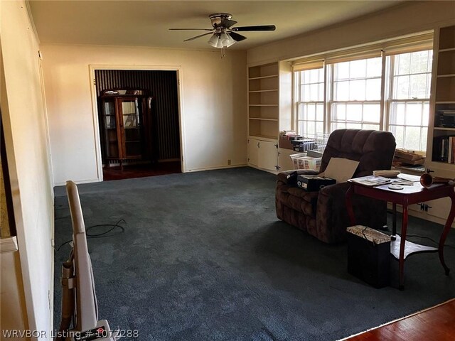 living area featuring built in shelves, dark carpet, and ceiling fan