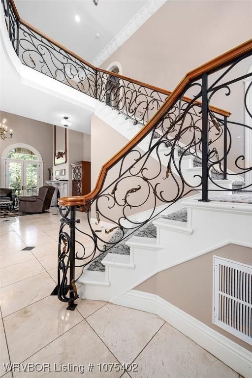 stairway featuring french doors, crown molding, a high ceiling, and an inviting chandelier