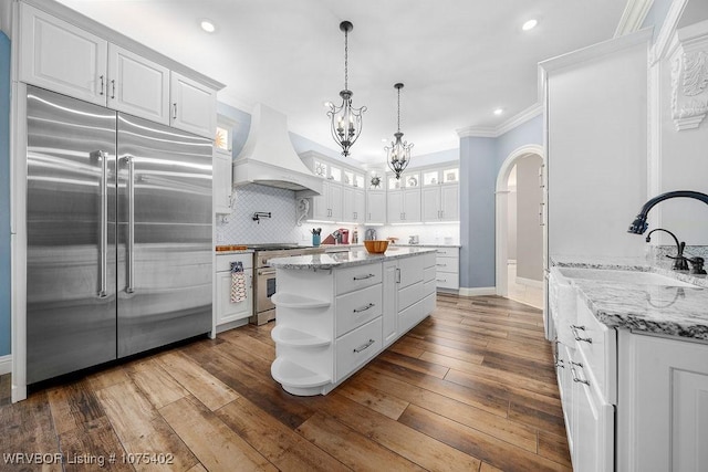 kitchen featuring white cabinets, custom range hood, high end appliances, and hardwood / wood-style floors