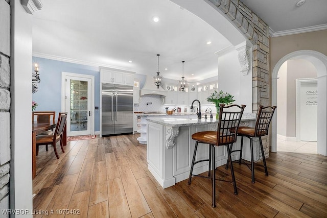 kitchen with light stone countertops, hanging light fixtures, built in fridge, light hardwood / wood-style floors, and white cabinets