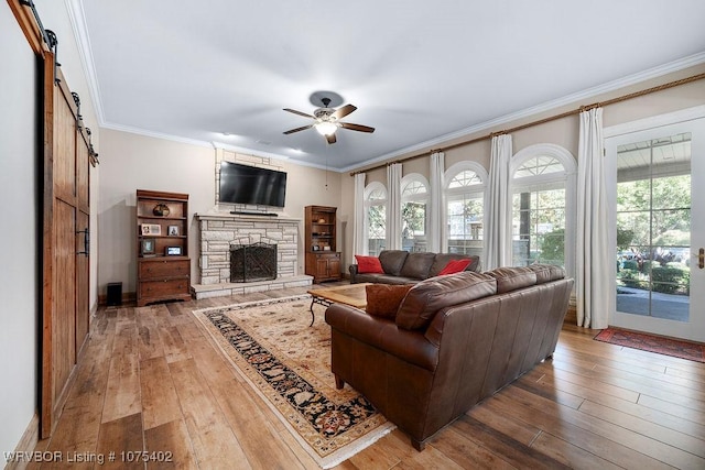 living room with ceiling fan, a barn door, crown molding, a fireplace, and hardwood / wood-style flooring