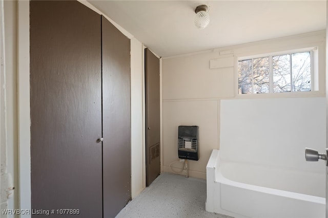 bathroom with heating unit and a bathtub