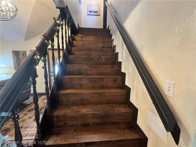 stairway featuring hardwood / wood-style flooring, a textured ceiling, and an inviting chandelier