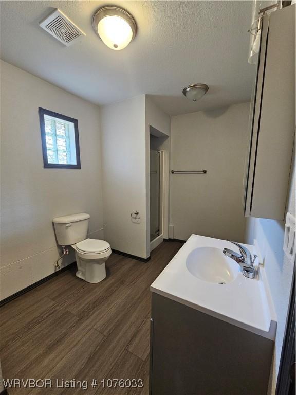 bathroom with walk in shower, vanity, a textured ceiling, wood-type flooring, and toilet