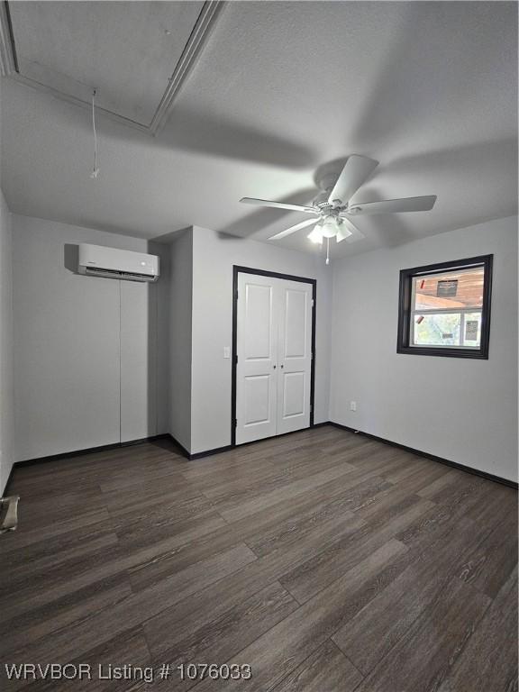 unfurnished bedroom featuring a wall mounted AC, dark hardwood / wood-style floors, and ceiling fan