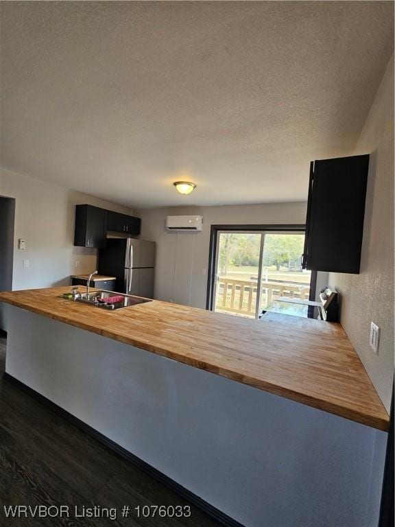 kitchen with wooden counters, an AC wall unit, stainless steel fridge, dark hardwood / wood-style flooring, and kitchen peninsula