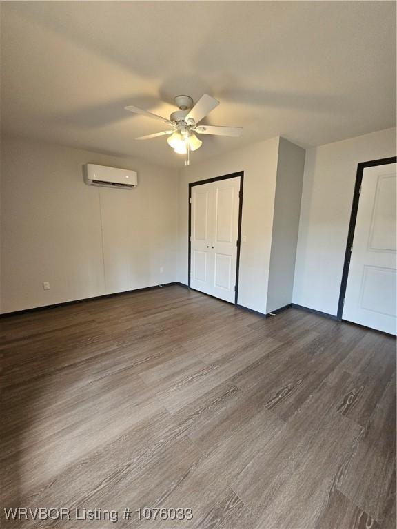 unfurnished bedroom with hardwood / wood-style floors, a closet, a wall unit AC, and ceiling fan