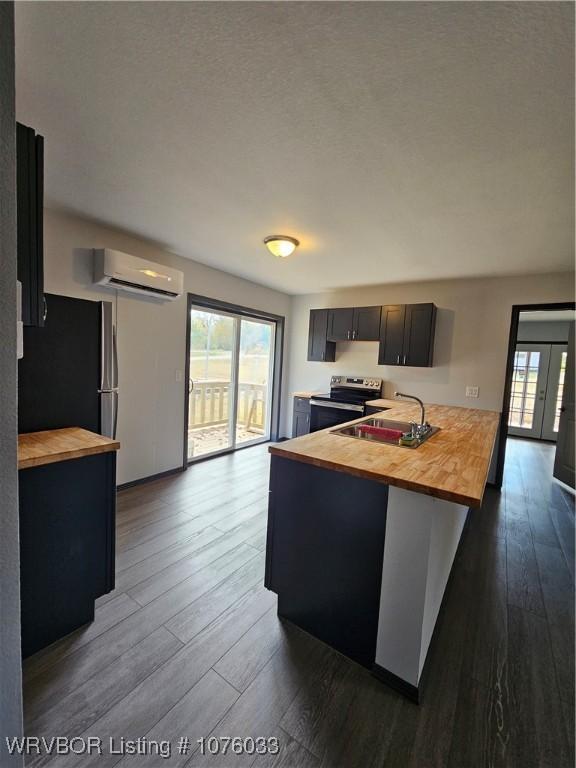 kitchen with stainless steel electric stove, wood counters, sink, and a wall unit AC