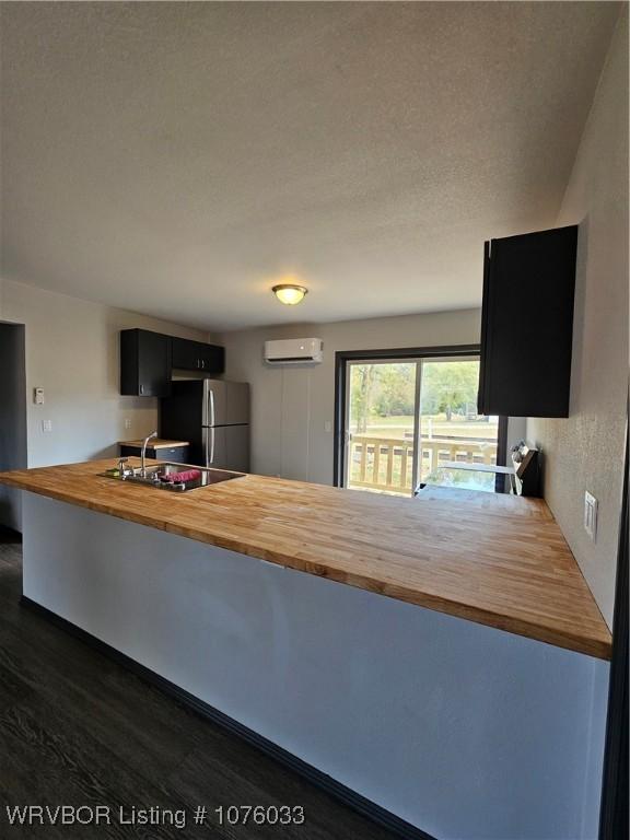 kitchen with wood counters, kitchen peninsula, a wall unit AC, sink, and stainless steel refrigerator