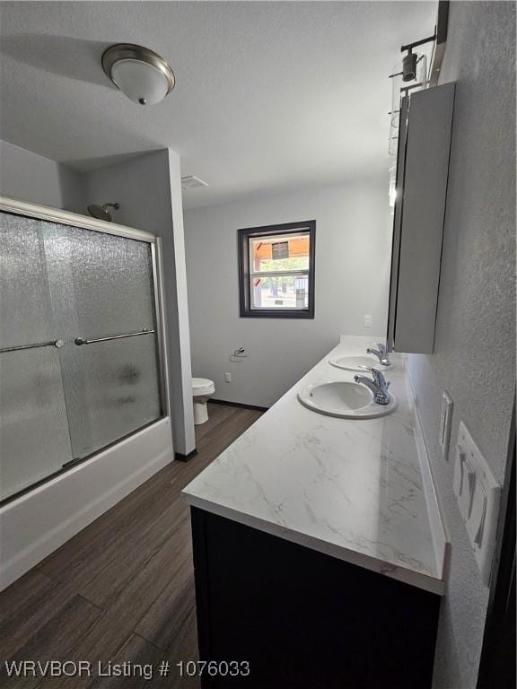 full bathroom featuring bath / shower combo with glass door, wood-type flooring, a textured ceiling, toilet, and vanity