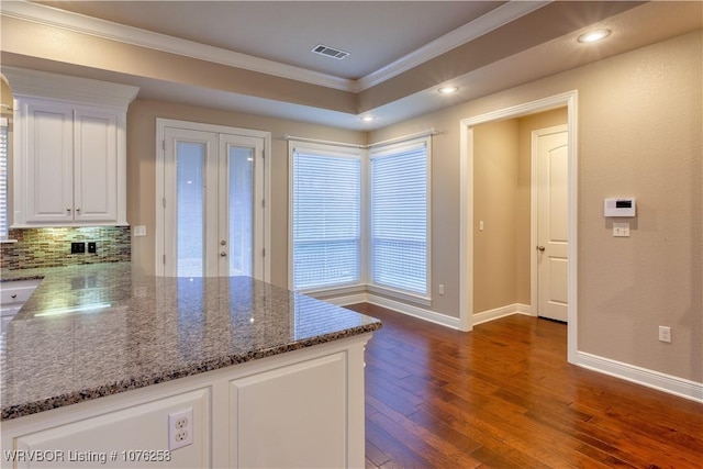 kitchen featuring backsplash, white cabinets, dark stone countertops, ornamental molding, and dark hardwood / wood-style flooring