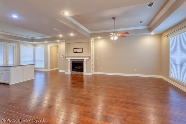 unfurnished living room featuring a tray ceiling, ceiling fan, a healthy amount of sunlight, and dark hardwood / wood-style floors