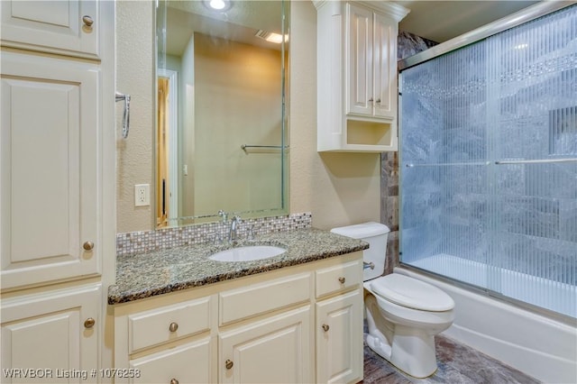 full bathroom featuring tasteful backsplash, vanity, bath / shower combo with glass door, and toilet