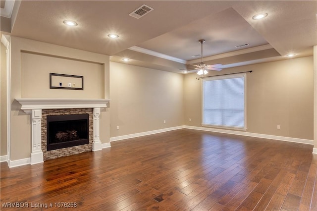 unfurnished living room with dark hardwood / wood-style floors, a raised ceiling, ceiling fan, and a stone fireplace