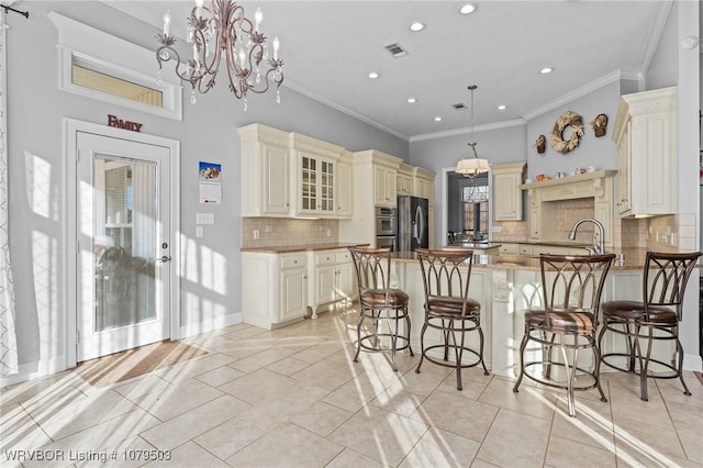 kitchen featuring crown molding, appliances with stainless steel finishes, a peninsula, an inviting chandelier, and cream cabinetry