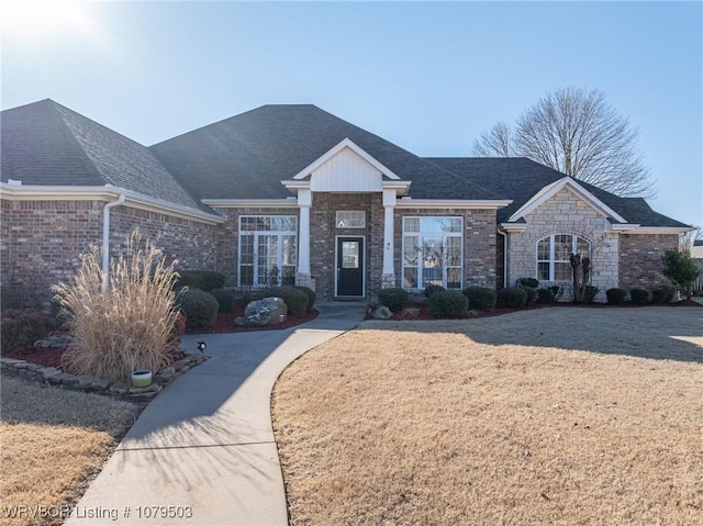 view of front of property featuring stone siding, a front lawn, and a shingled roof